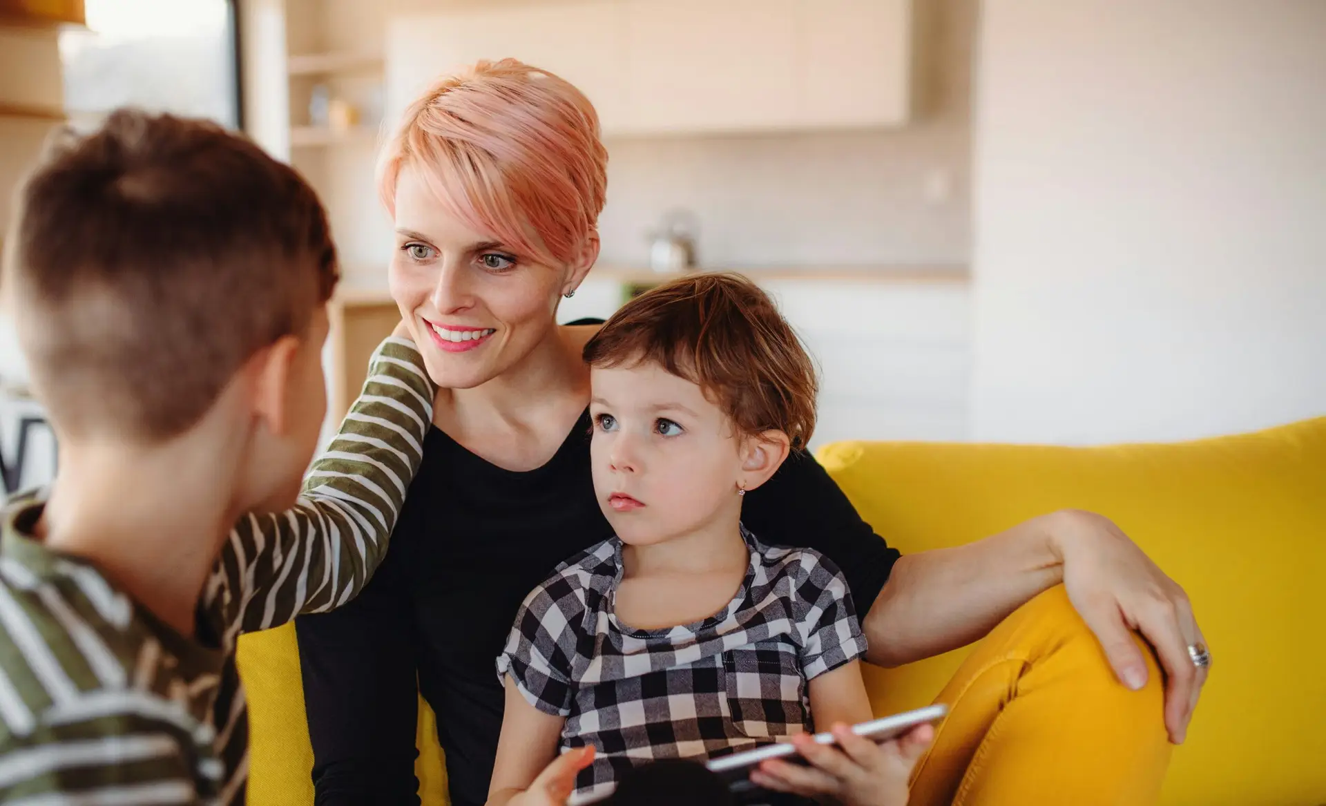 An adult and two children sitting together and looking at a tablet.